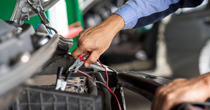 Professional car mechanic using jumper cables to start a car battery.